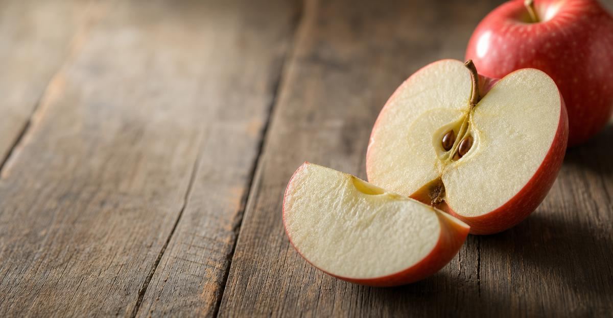 A close-up of a halved apple showing the contrast between the shiny red peel and the crisp white fruit flesh.