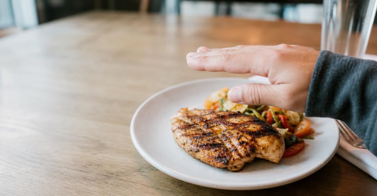 A person using their hand as a guide to estimate the portion size of a grilled chicken breast at a restaurant.