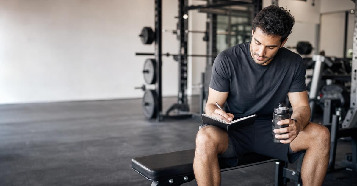 A person writing in a notebook while resting between sets at a gym.