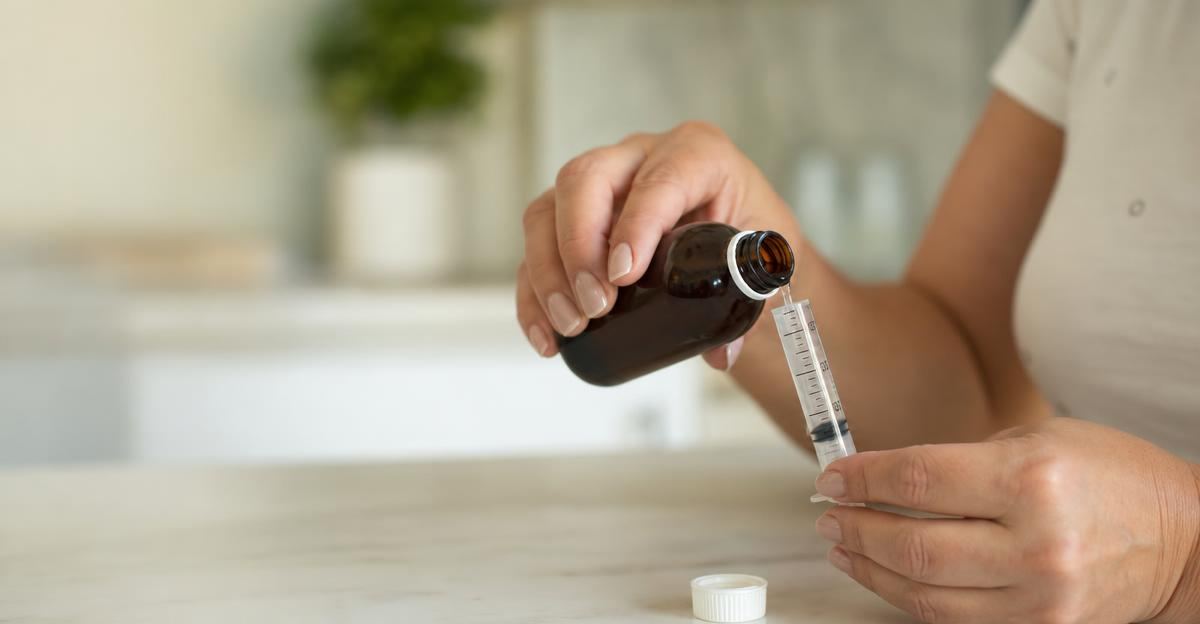 A person carefully measuring liquid medication into a syringe in a well-lit kitchen.